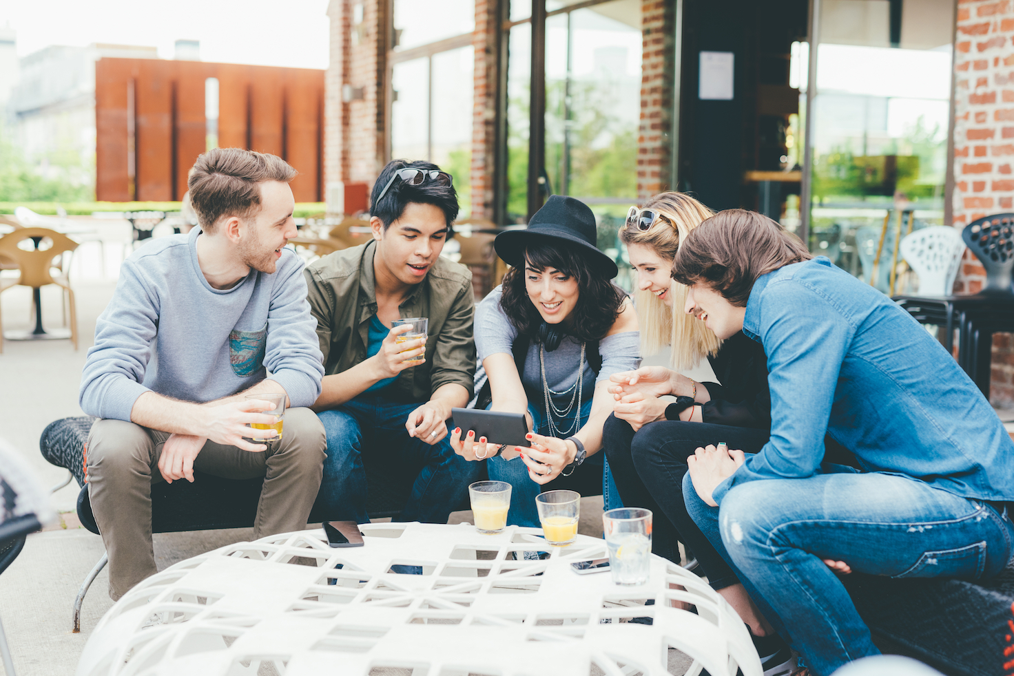 Group of friends millennials sitting outdoor in a bar using smart phone, having fun - interaction, togetherness, socializing concept